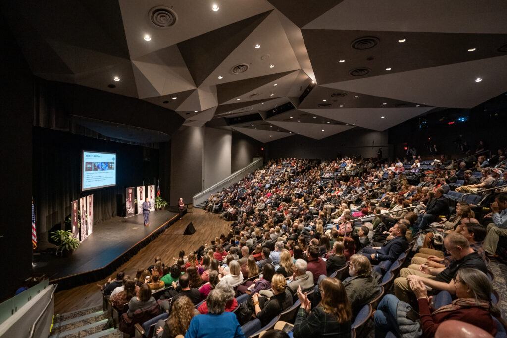 a photo of a crowd in Rudder Theatre with Interim President Mark A. Welsh III on the stage.
