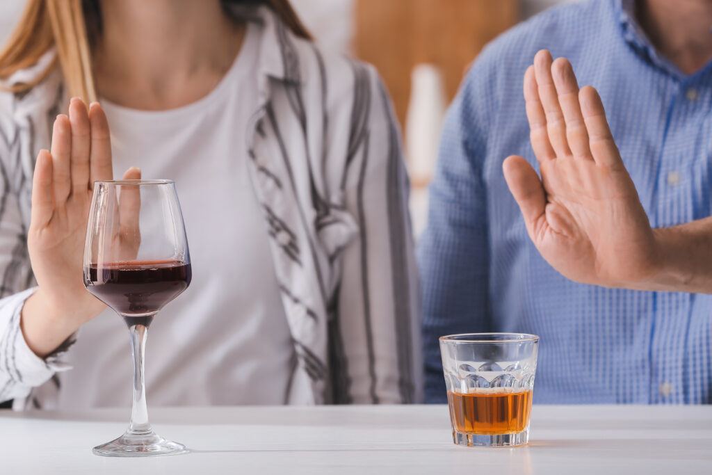 A photo of a couple with hands blocking alcoholic drinks.