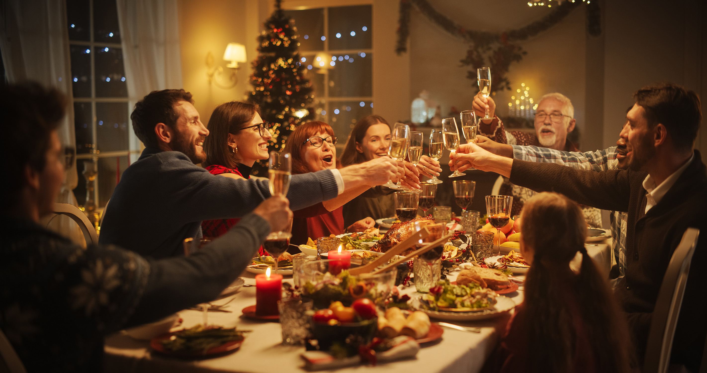 A photo of a family and friends at a Christmas dinner table celebrating a toast with raised glasses.