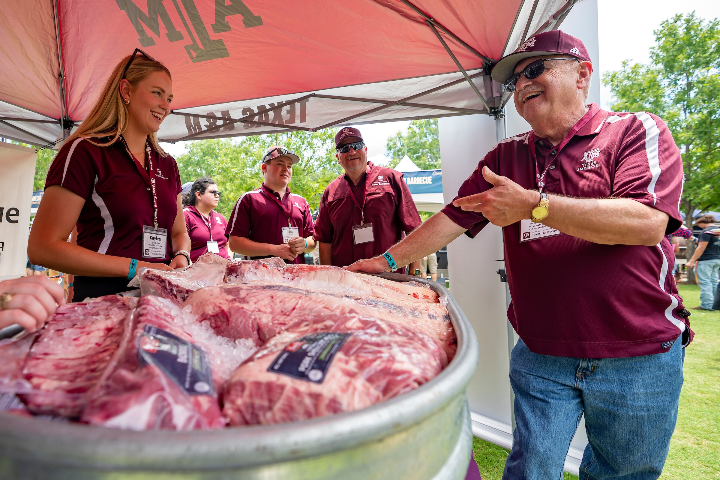 a photo of Jeff Savell in a Texas A&M baseball cap talking and laughing with students as they stand around a display of various packaged meats on ice