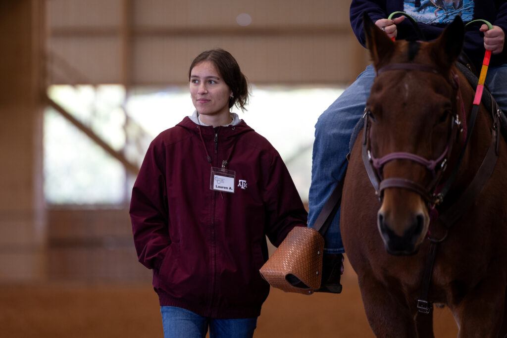 a photo of a young woman in a maroon Texas A&M jacket walking alongside a horse