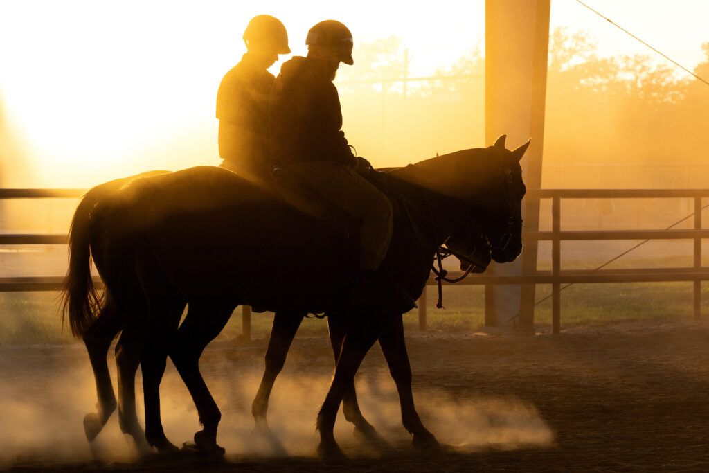 a photo of two people on horses silhouetted against the setting sun, as dust from the arena swirls around them