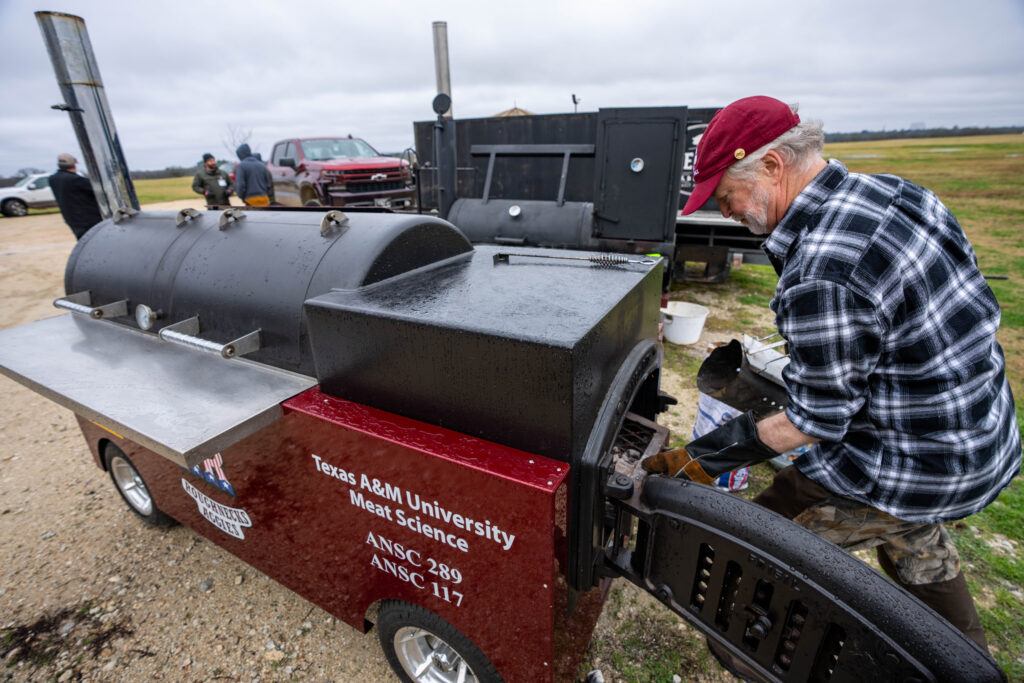 a photo of a man working with a smoker labeled "Texas A&M University Meat Science"