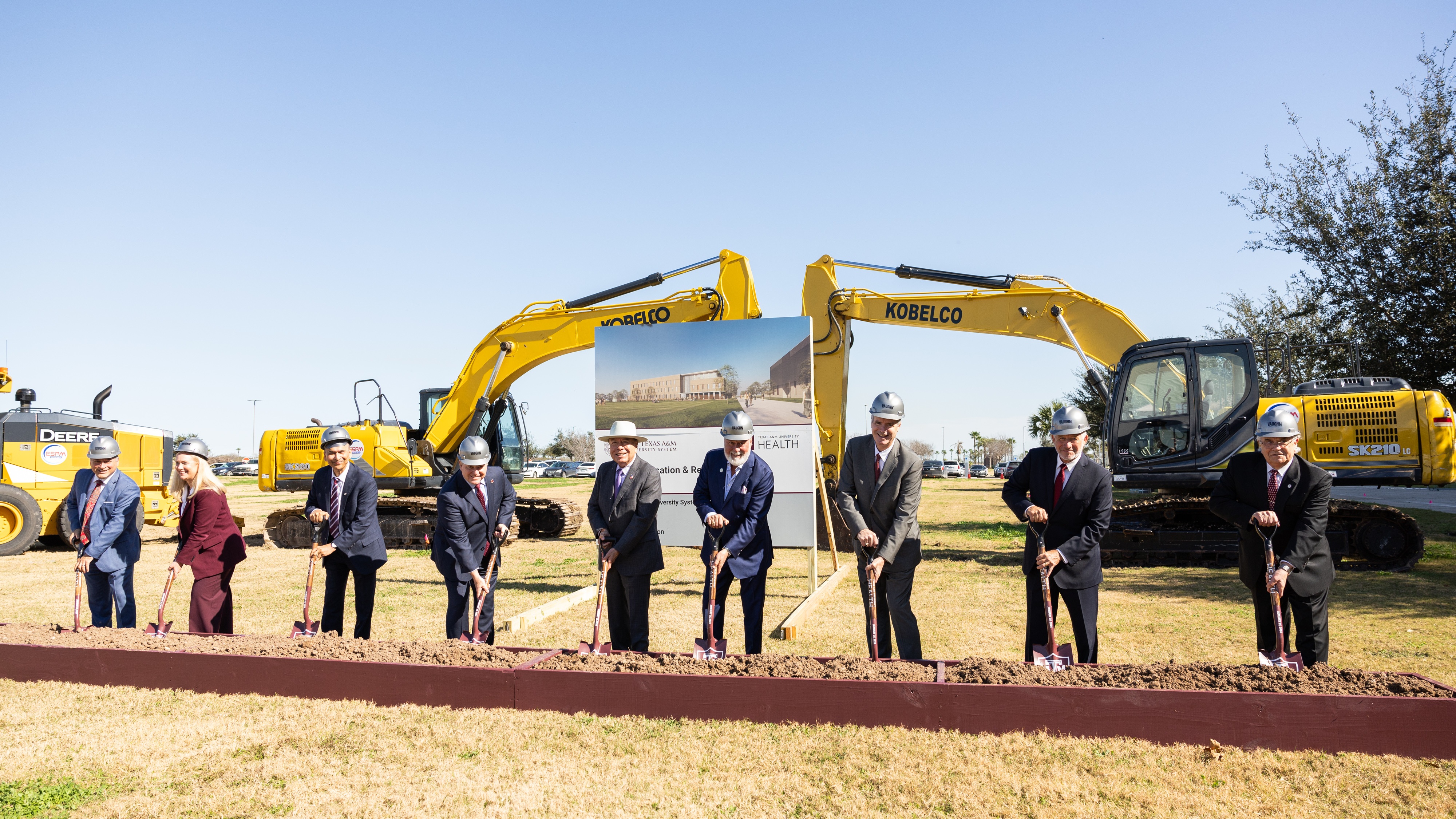 A photo of a group of people with shovels in front of heavy equipment for a groundbreaking ceremony.
