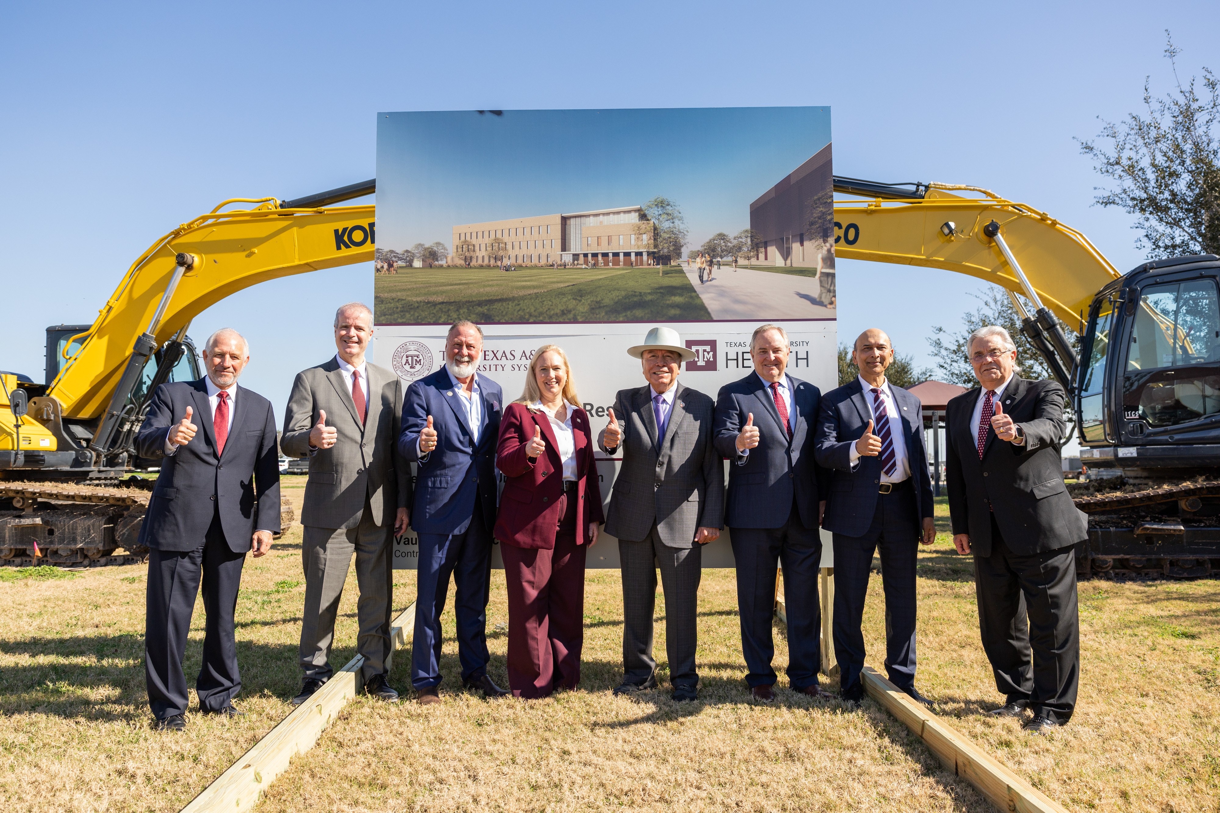 A photo of a group of people standing on the site of a future construction project, with heavy equipment and a rendering of the future building in the background.