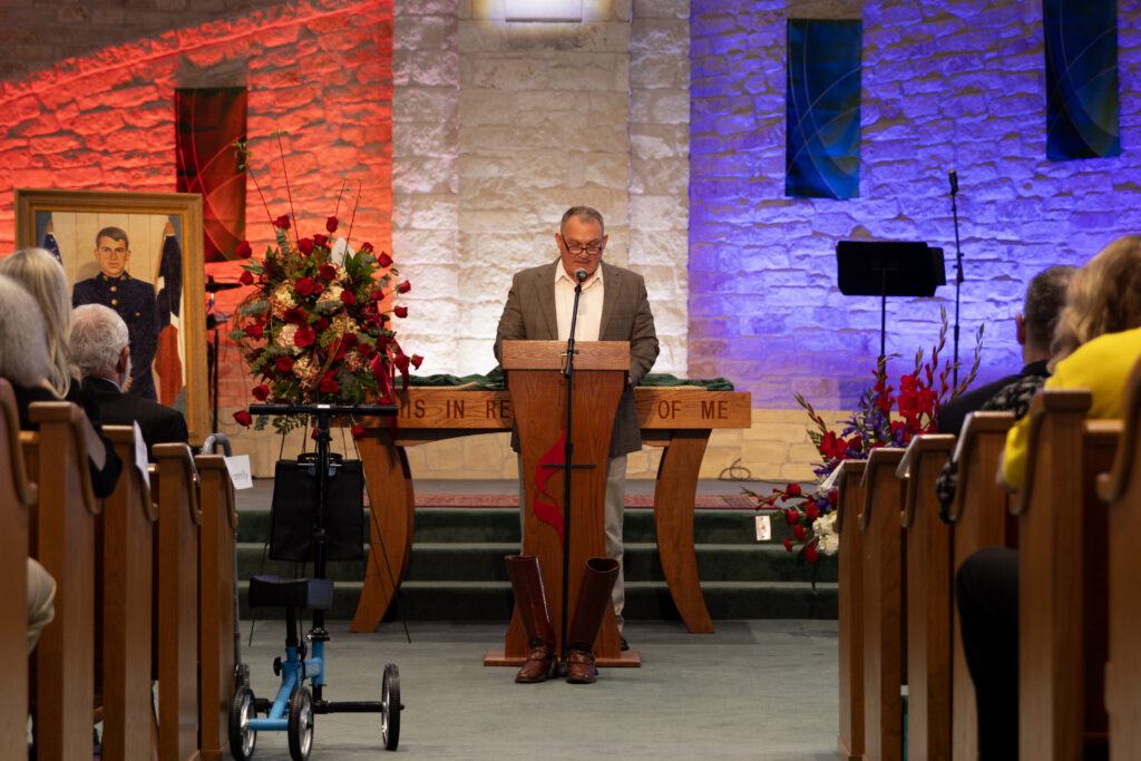 A photo of a man at a lectern in a church speaking during a memorial service.