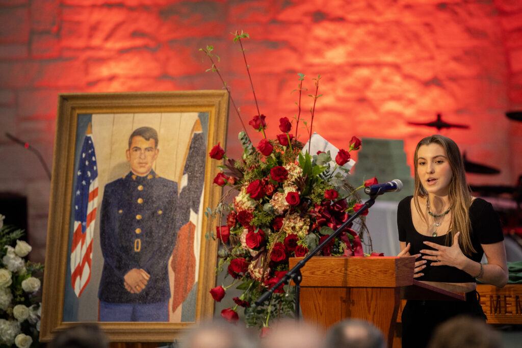 A photo of a woman at a lectern speaking at a memorial service.