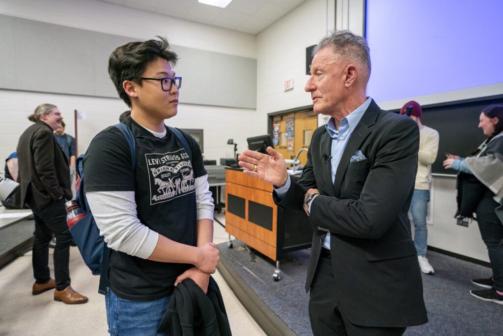 A photo of a man speaking to a student in a college classroom.