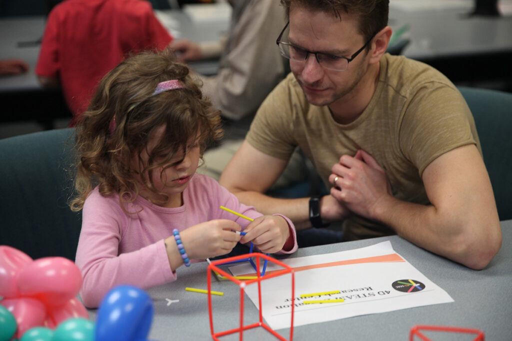 a child and her parent work on an activity at a previous fair event