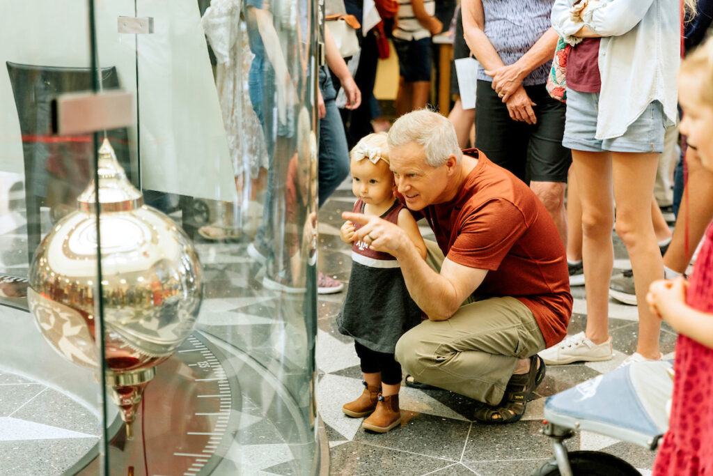 a man showing a toddler the pendulum in the Mitchell Physics Building foyer