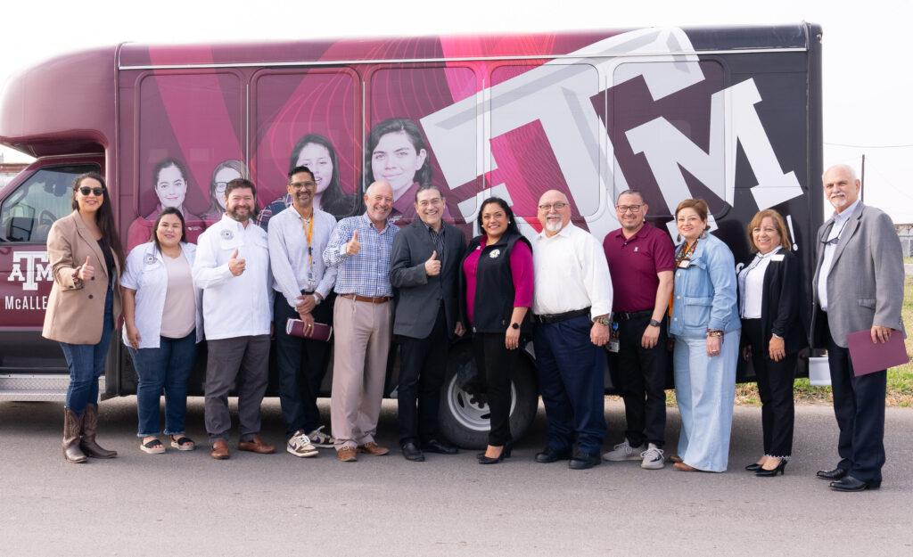 Santos, center, flashes a Gig 'em with McAllen center staff and area officials in front of the bus they took to the colonia
