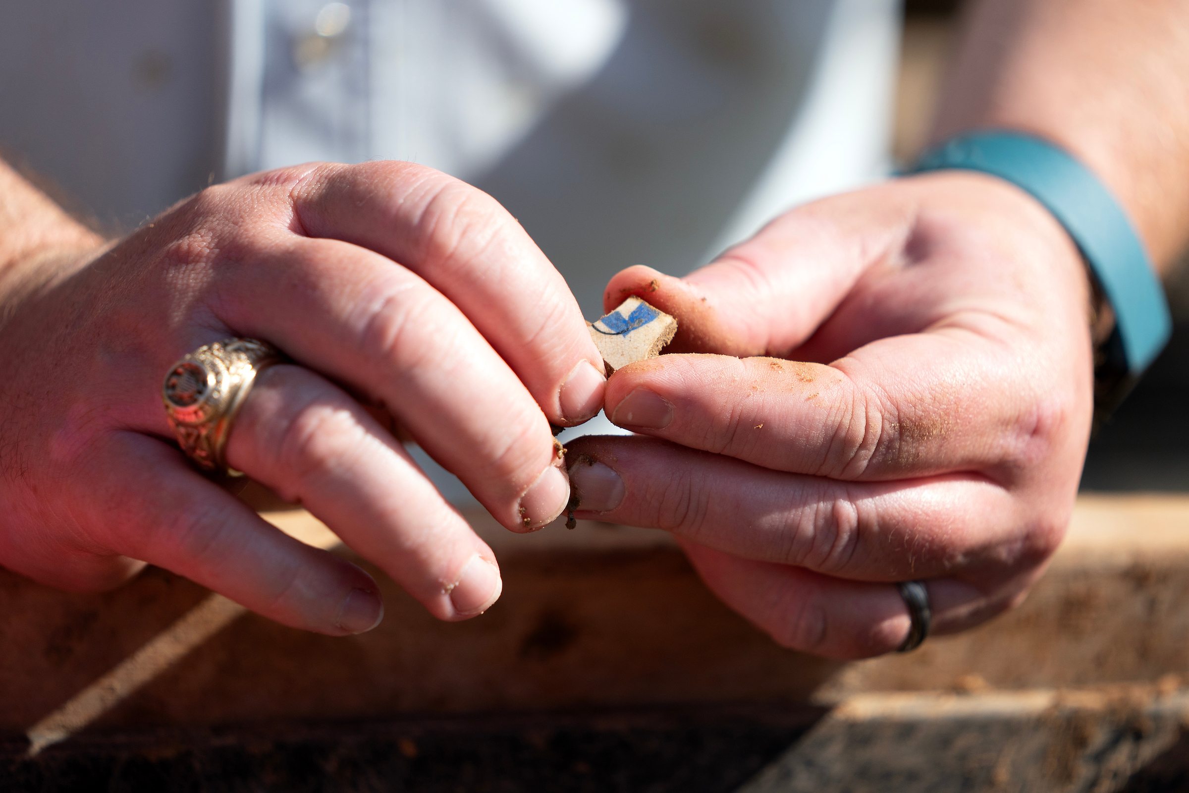 a man with an Aggie Ring holds a small chunk of painted pottery in his fingers