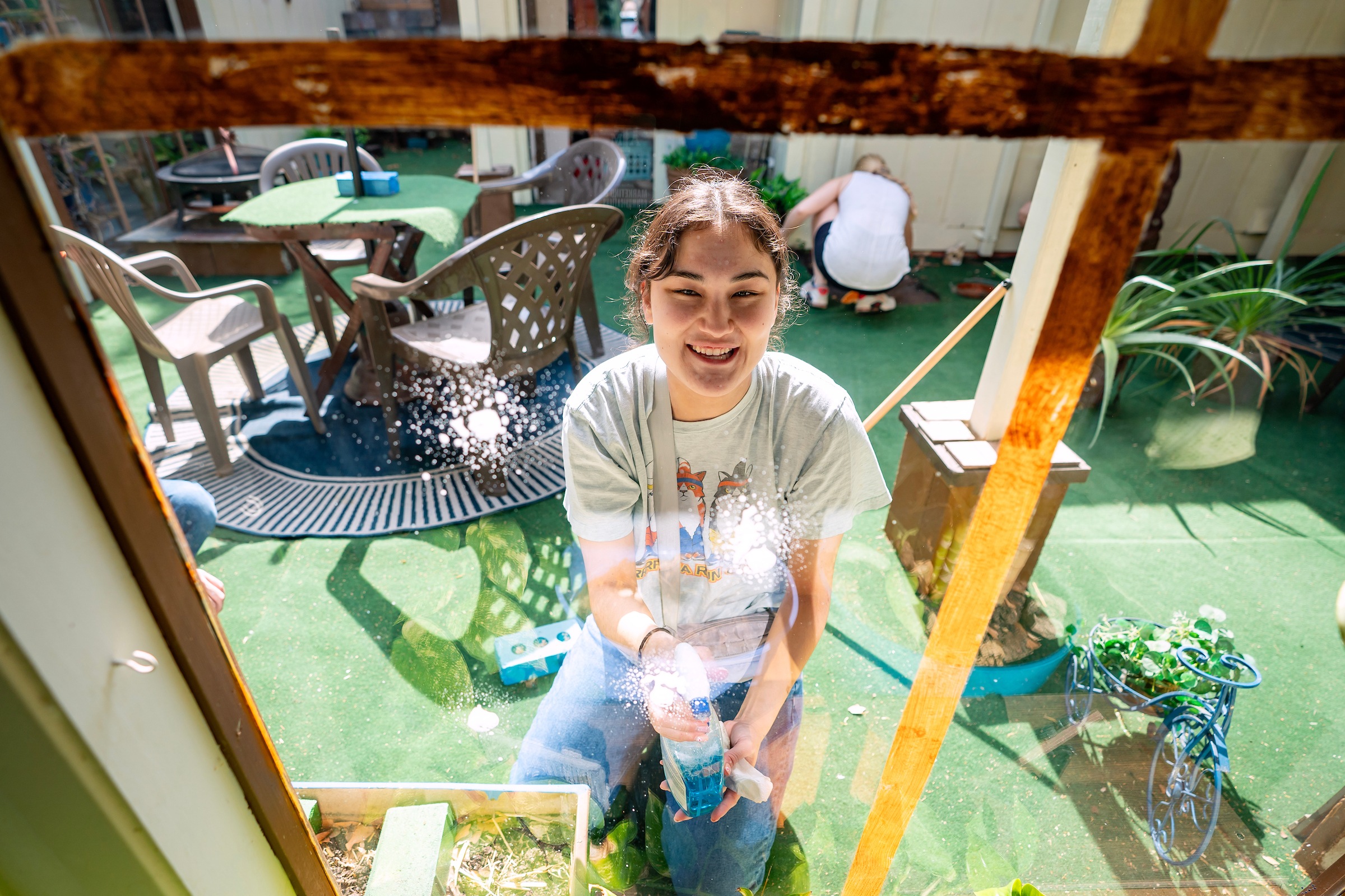 a young woman smiles while spraying glass cleaner on a window