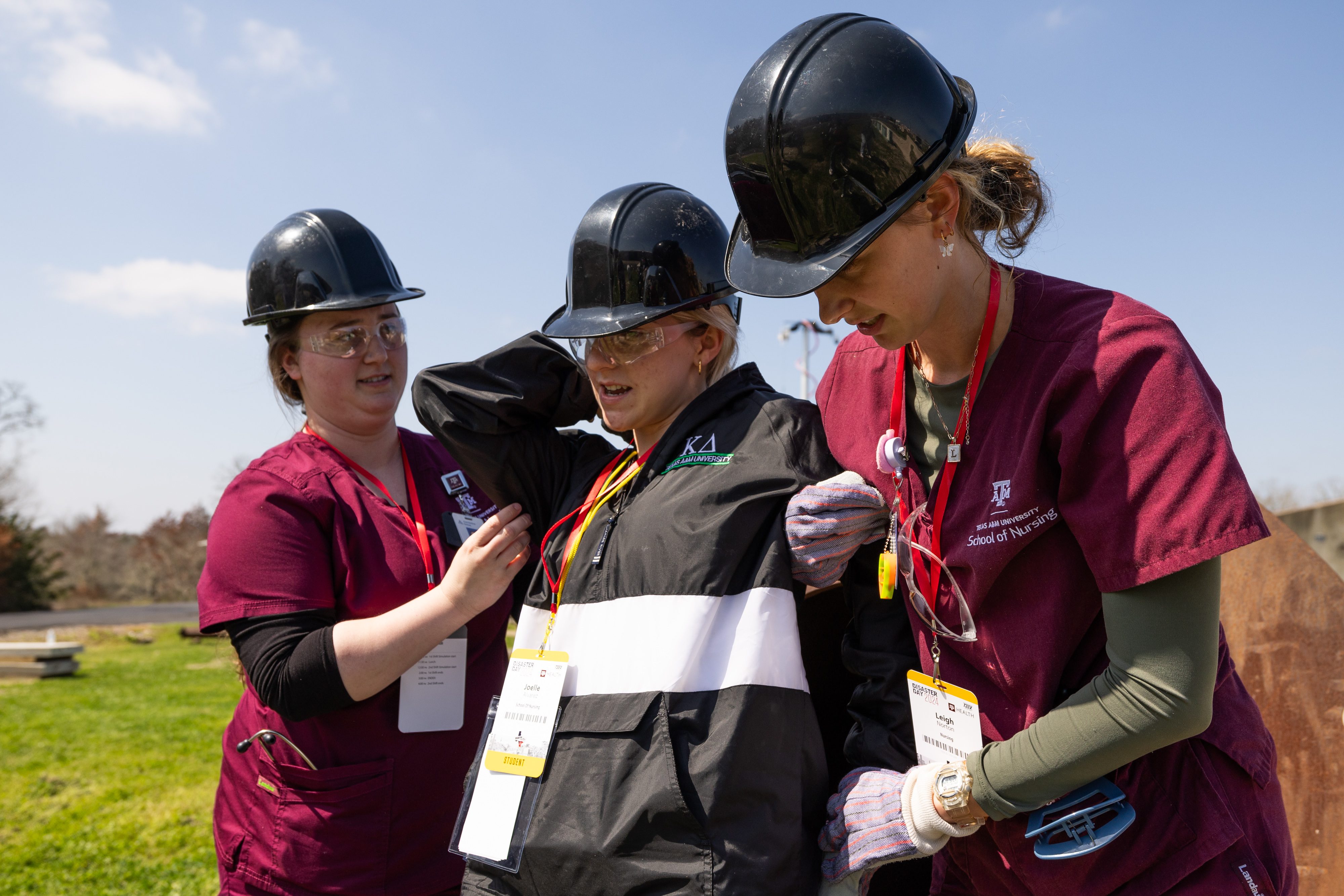 Two people wearing hard hats help a third person who is acting as a victim during a disaster training exercise.