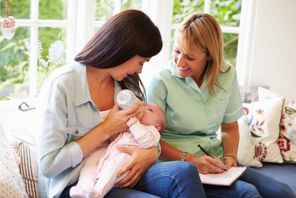 A photo of a mother with a baby meeting with a health visitor at her home.