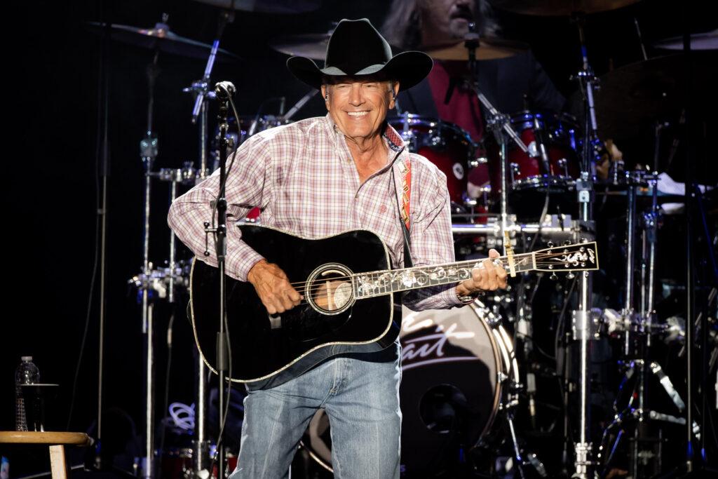 A photo of a singer holding a guitar on stage during a concert.