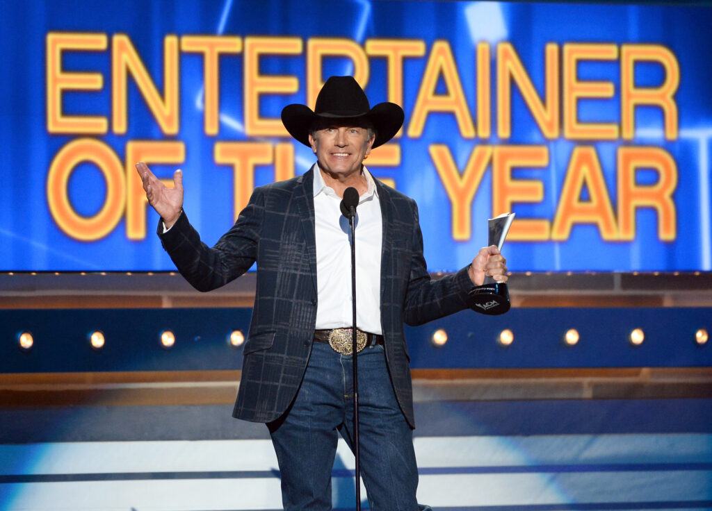 A photo of a singer accepting an award with the words Entertainer of the Year on a screen in the background.
