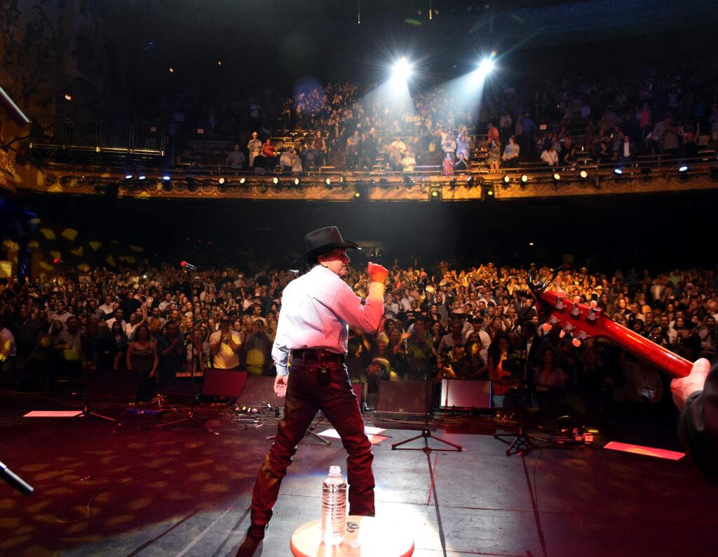A photo of an entertainer on a stage from the back of the stage showing the cheering audience.