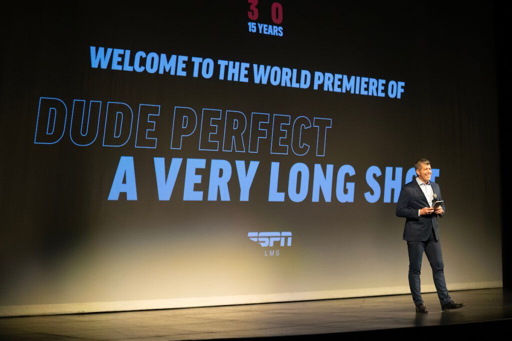 Fernando Palomo addressing the audience before the documentary screening. Behind him, the screen says "Welcome to the world premiere of Dude Perfect A Very Long Shot" ESPN Films