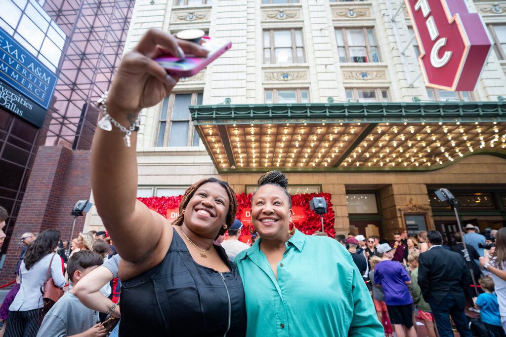 Two adult fans taking a selfie on the red carpet.