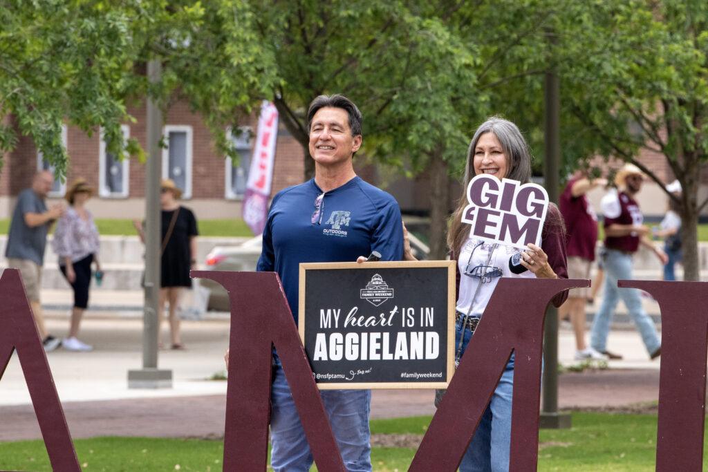 A man and a woman holding signs for a photo during Family Weekend on the Texas A&M campus.