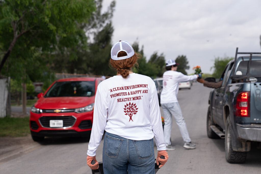 a student volunteer pushing a wheelbarrow with a shirt that says "A clean environment promotes a happy and healthy mind/"