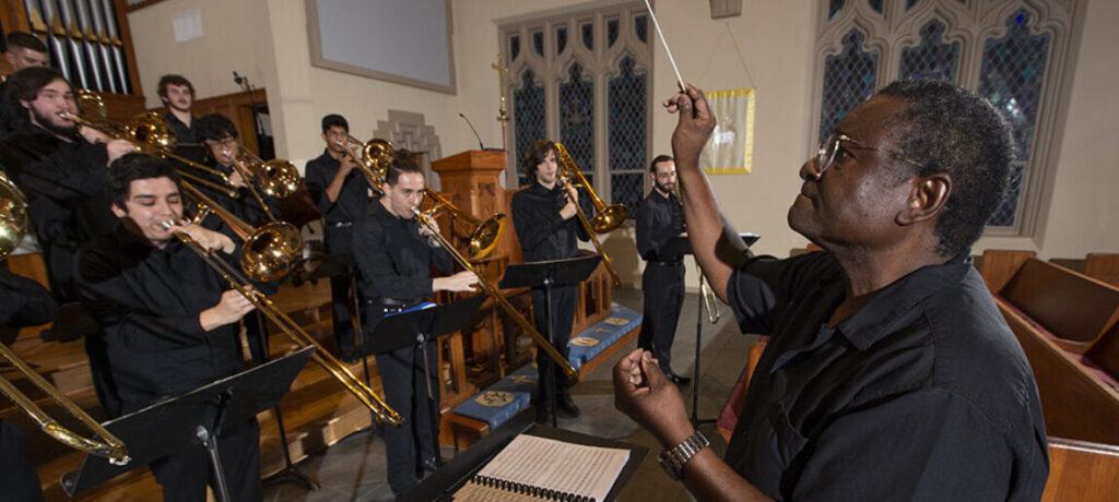 A conductor leading a trombone choir in a church.