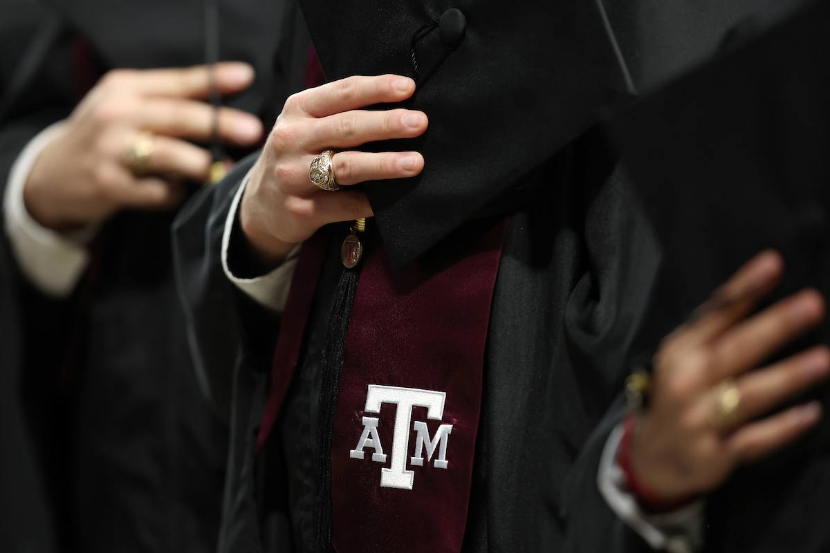 a photo of a hand with an Aggie ring grasping a mortarboard with a Texas A&M stole below