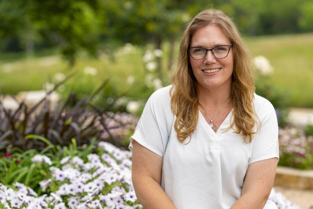 Portrait of Dara Wald sitting outdoors in front of a bed of flowers in the background