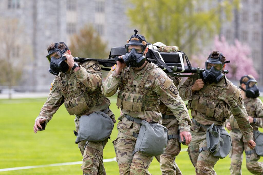 A group of cadets wearing combat fatigues and gas masks competes in an event during a military skills competition.