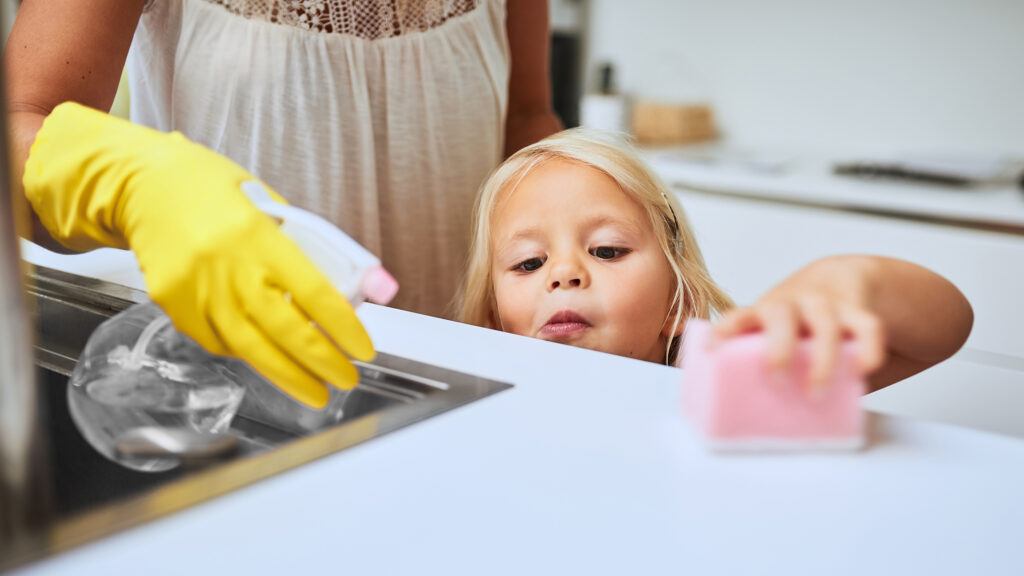 A mother and her young daughter cleaning a kitchen surface together at home.