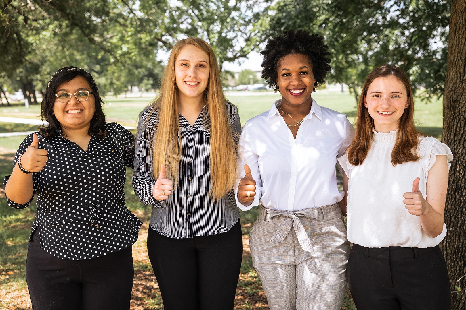 Four women posing for a photo outside under trees.
