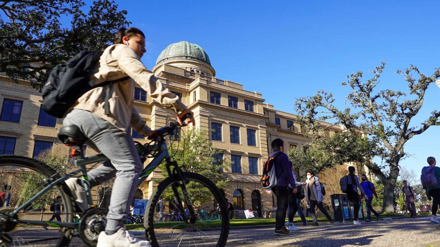 A student rides a bike past the Academic Building on the Texas A&M University campus.