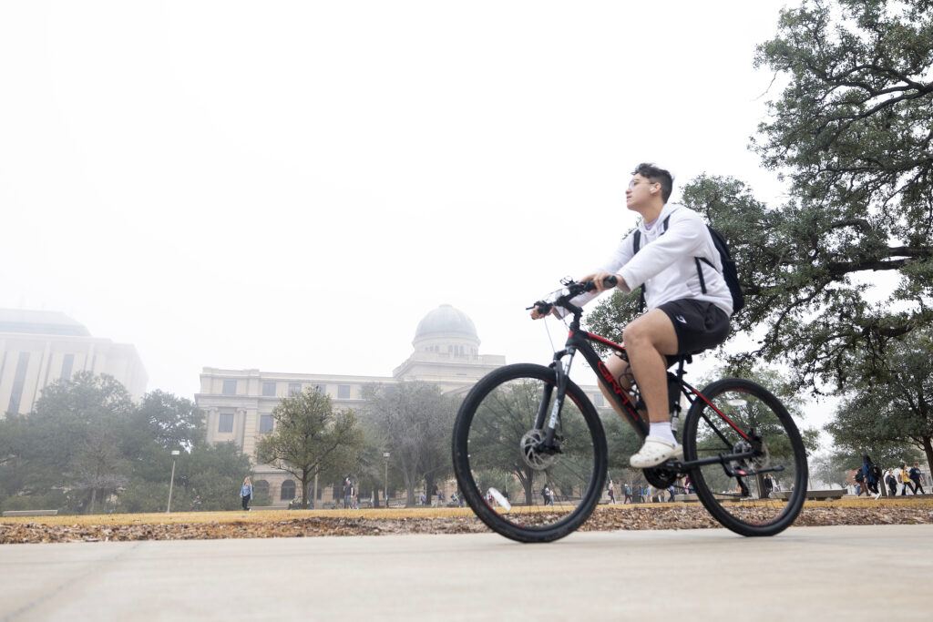 A student rides a bike past the Academic Building on the Texas A&M University campus on a foggy day.