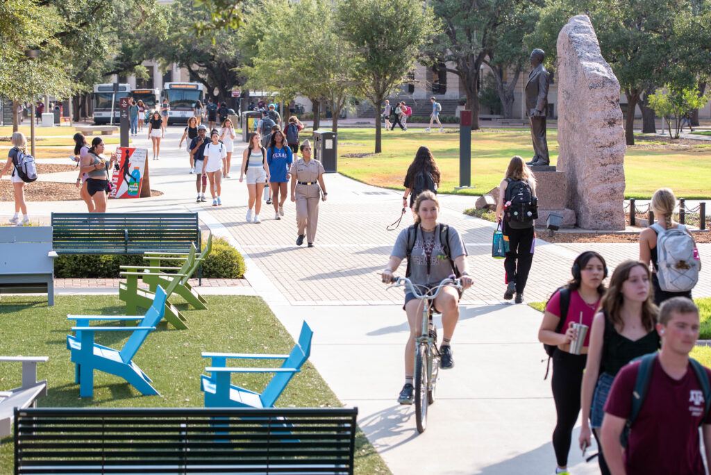 A bicycle rider navigates a sidewalk full of pedestrians on the Texas A&M University campus.