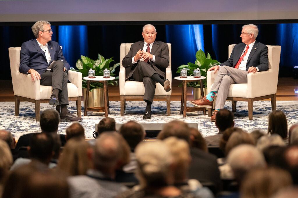 Jeb Bush, Robert Gates and Andrew Card seated on a stage as they speak before an audience.