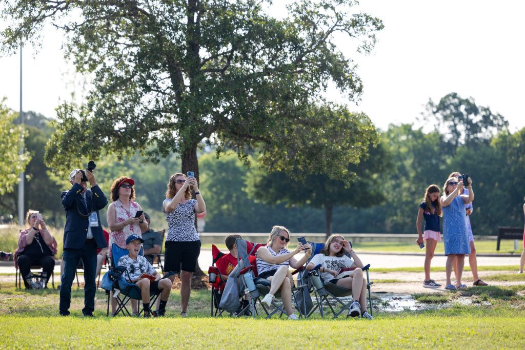 people in chairs and standing on grass look up to the sky and take photos