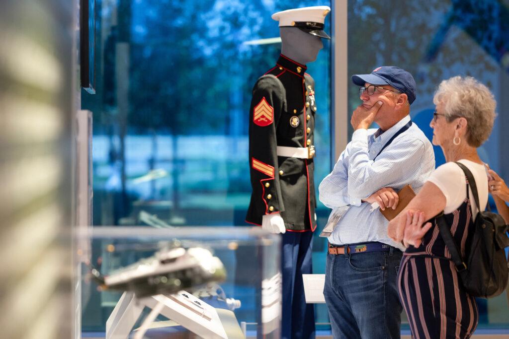 two people look at a museum exhibit. a mannequin in a Marines dress uniform stands in the background