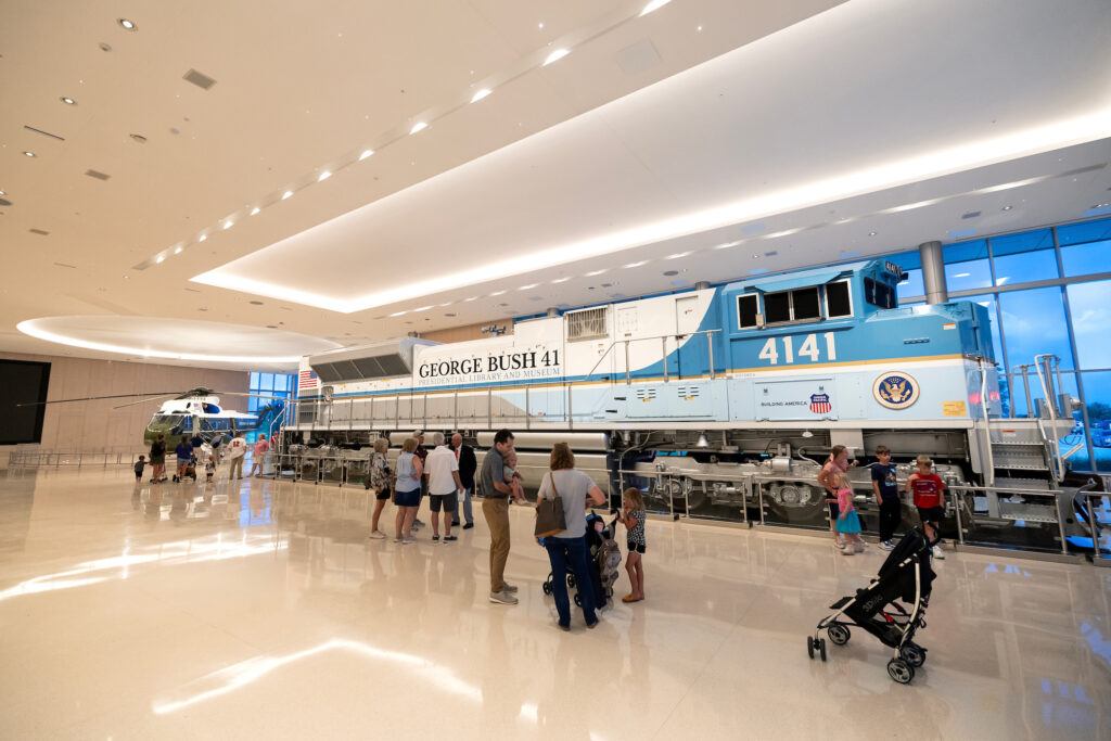 a group of people look at the 4141 Locomotive with Marine One in the background