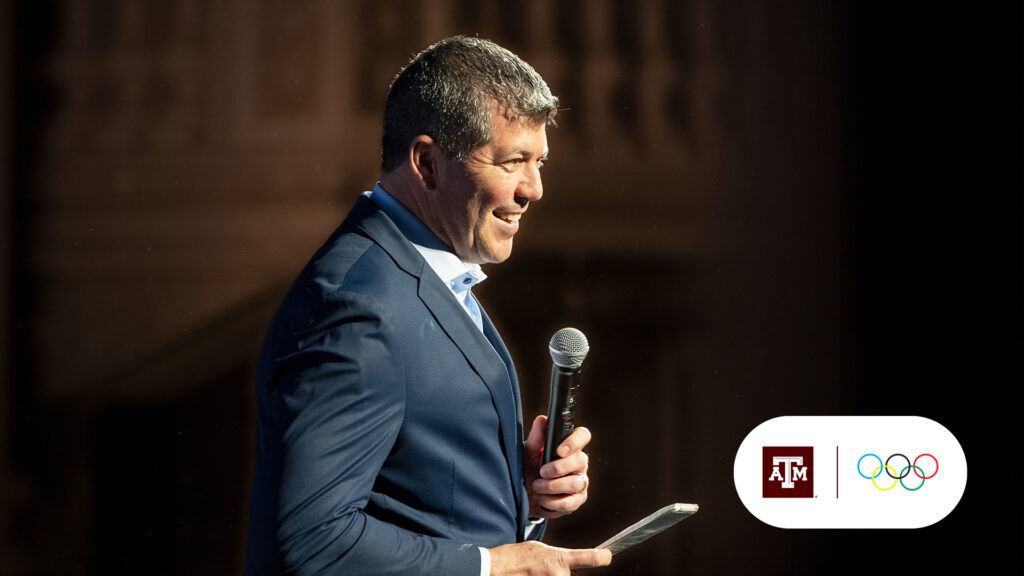 A photo of Fernando Palomo speaking on stage with the Texas A&M and Olympic Games logos added to the corner of the image.