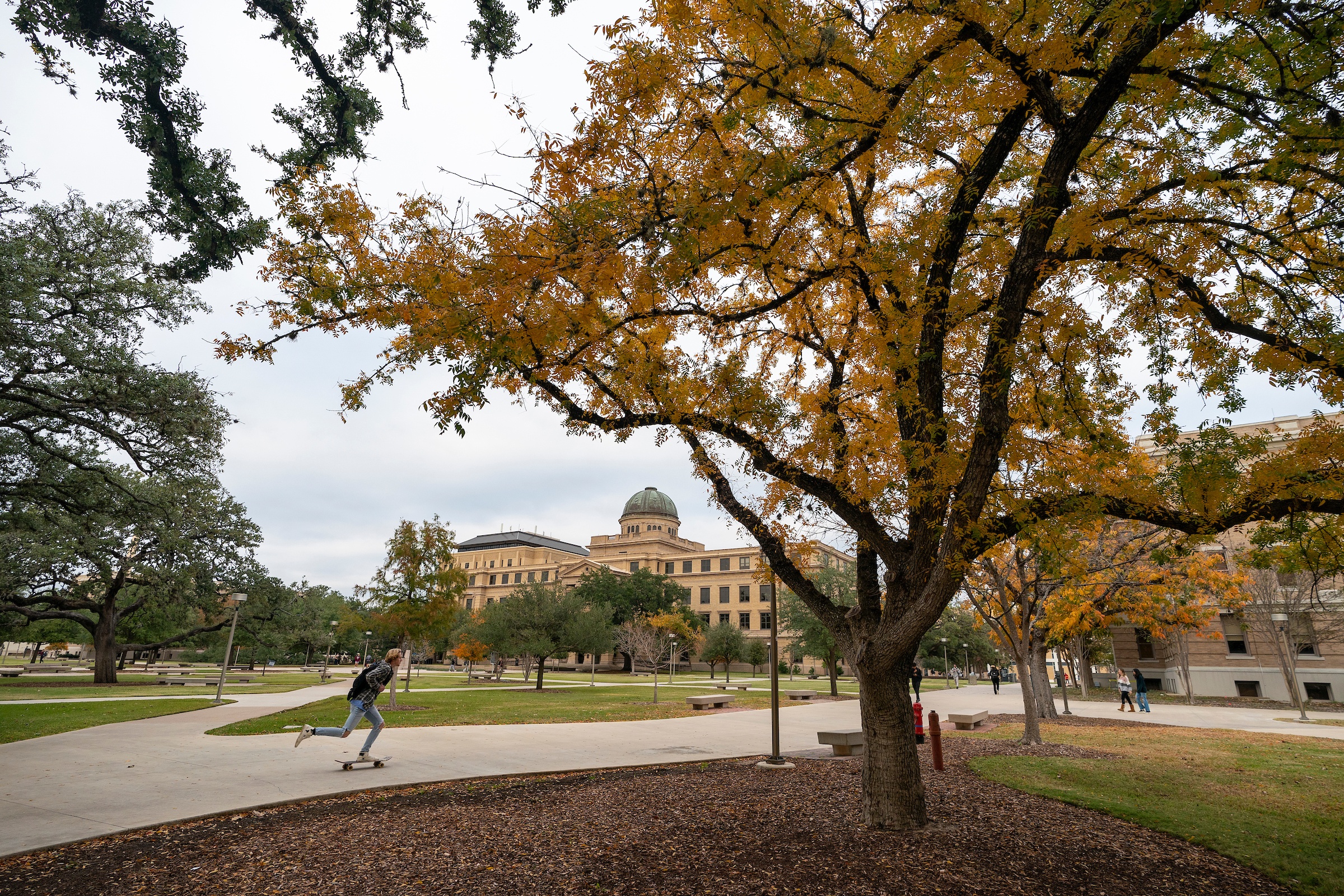 A student rides a skateboard past the Academic Building on the Texas A&M University campus during the fall.