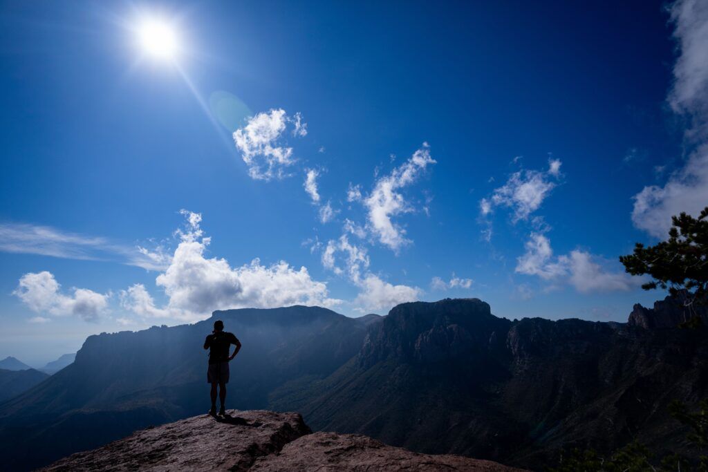 a photo of a person standing on a mountaintop with the blazing sun overhead
