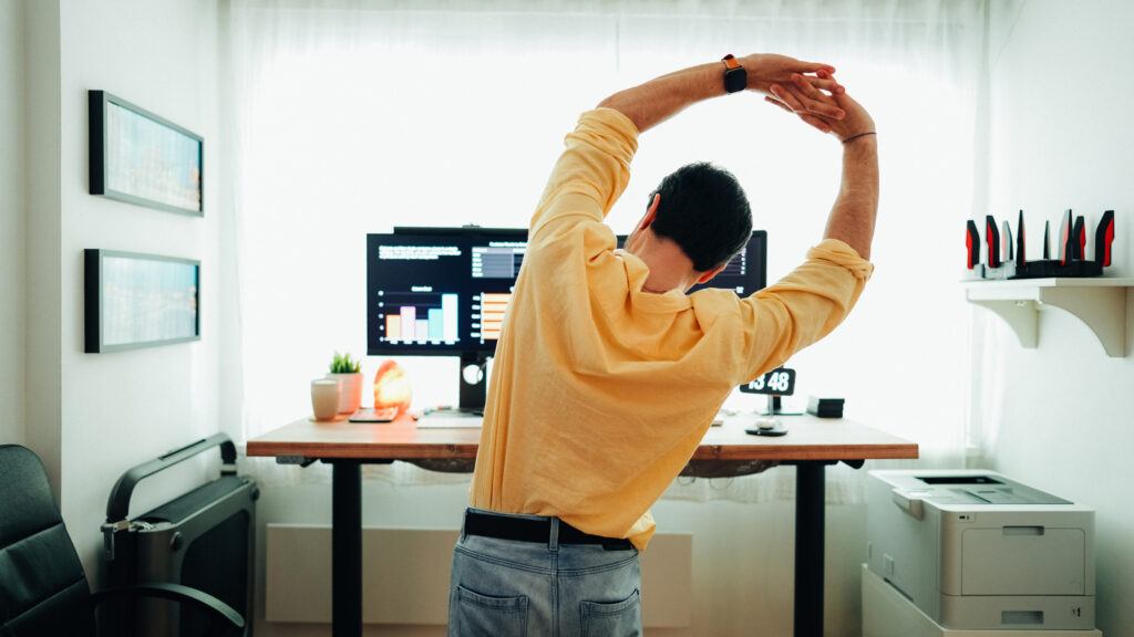 Man working at home stretching in front of a standing desk