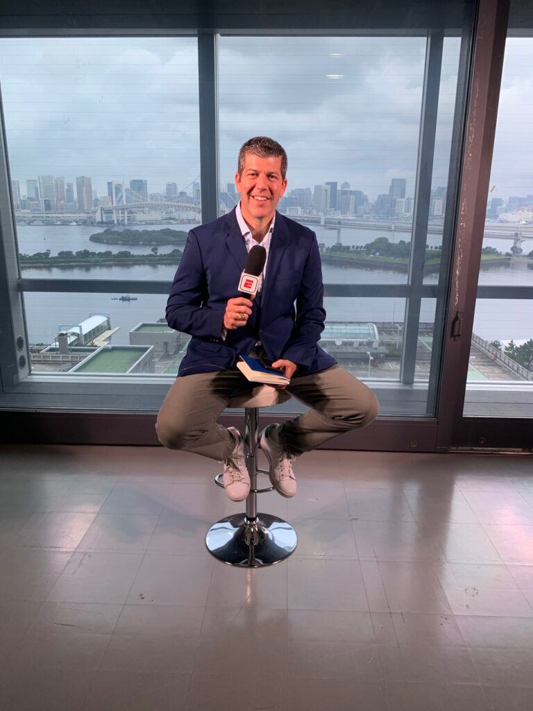 a photo of Fernando Palomo holding a microphone in front of the Tokyo skyline at the 2020 olympics