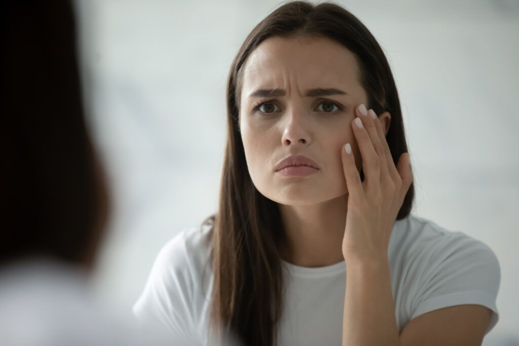 Close up head shot of an unhappy young woman checking skin