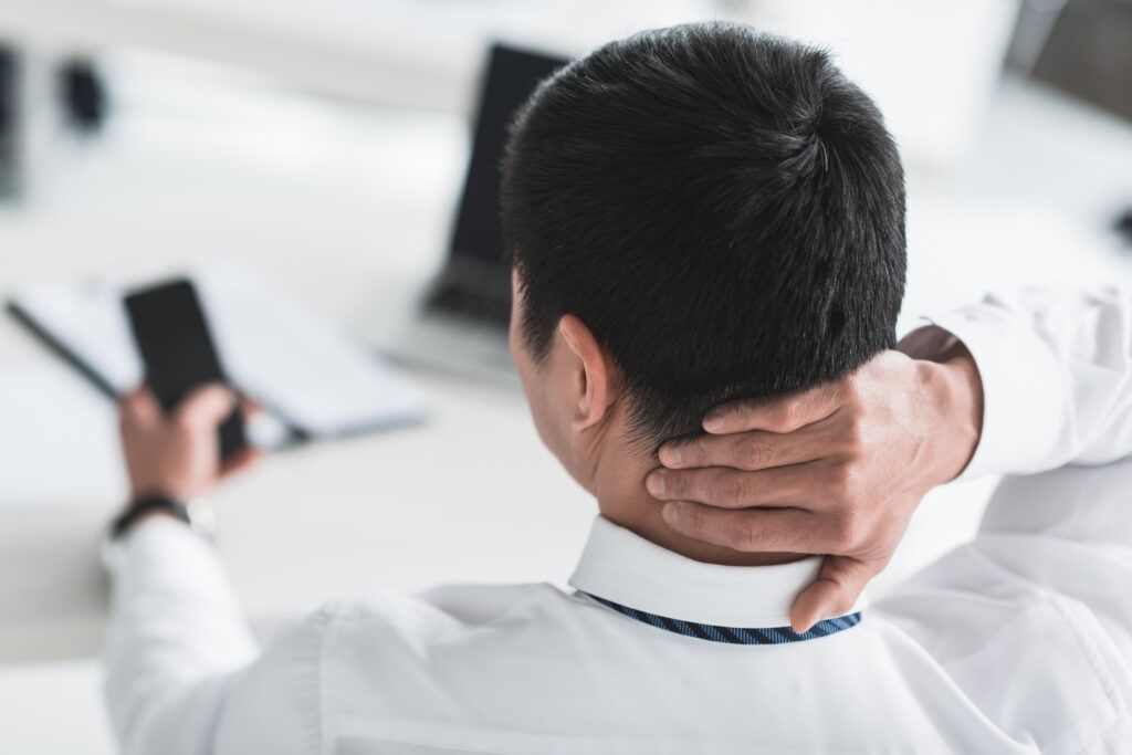 a man with his hand on his neck as he looks at his cell phone