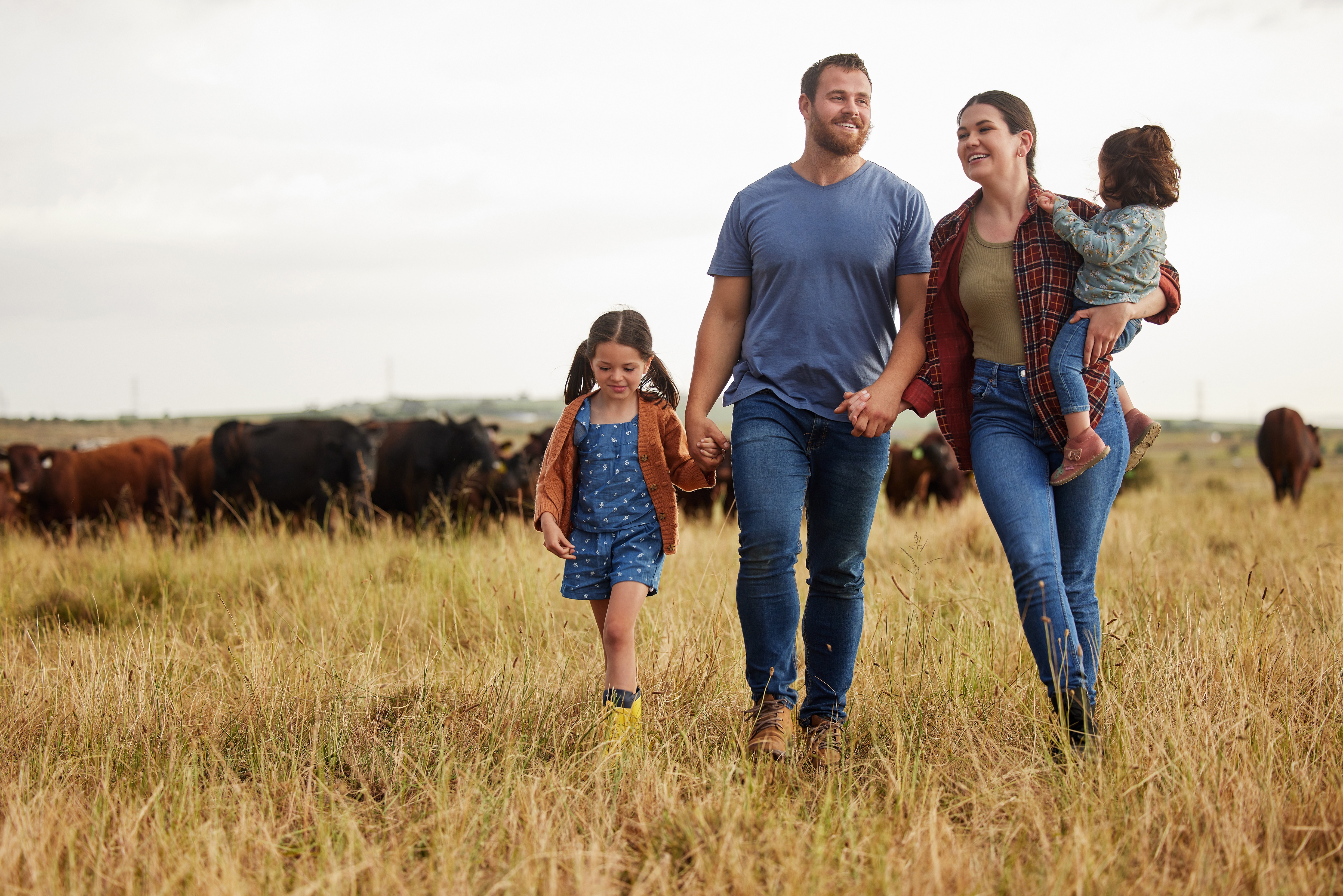 A rural family — a man, woman and two young children — walking in a pasture with cattle in the background.