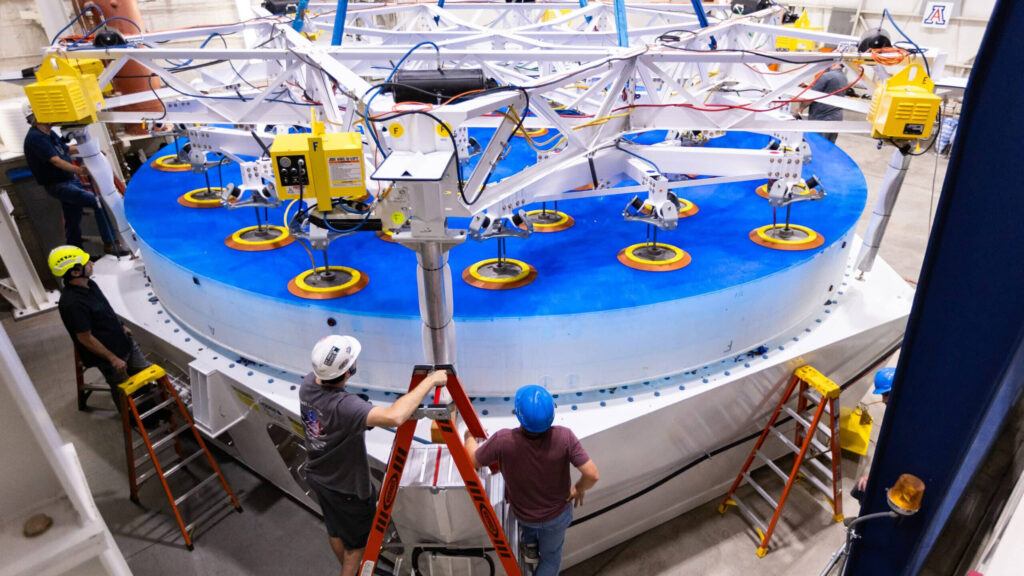 Completed 8.4-meter-diameter primary mirror, installed into its support system prototype with technicians in the foreground at the University of Arizona’s Richard F. Caris Mirror Lab.
