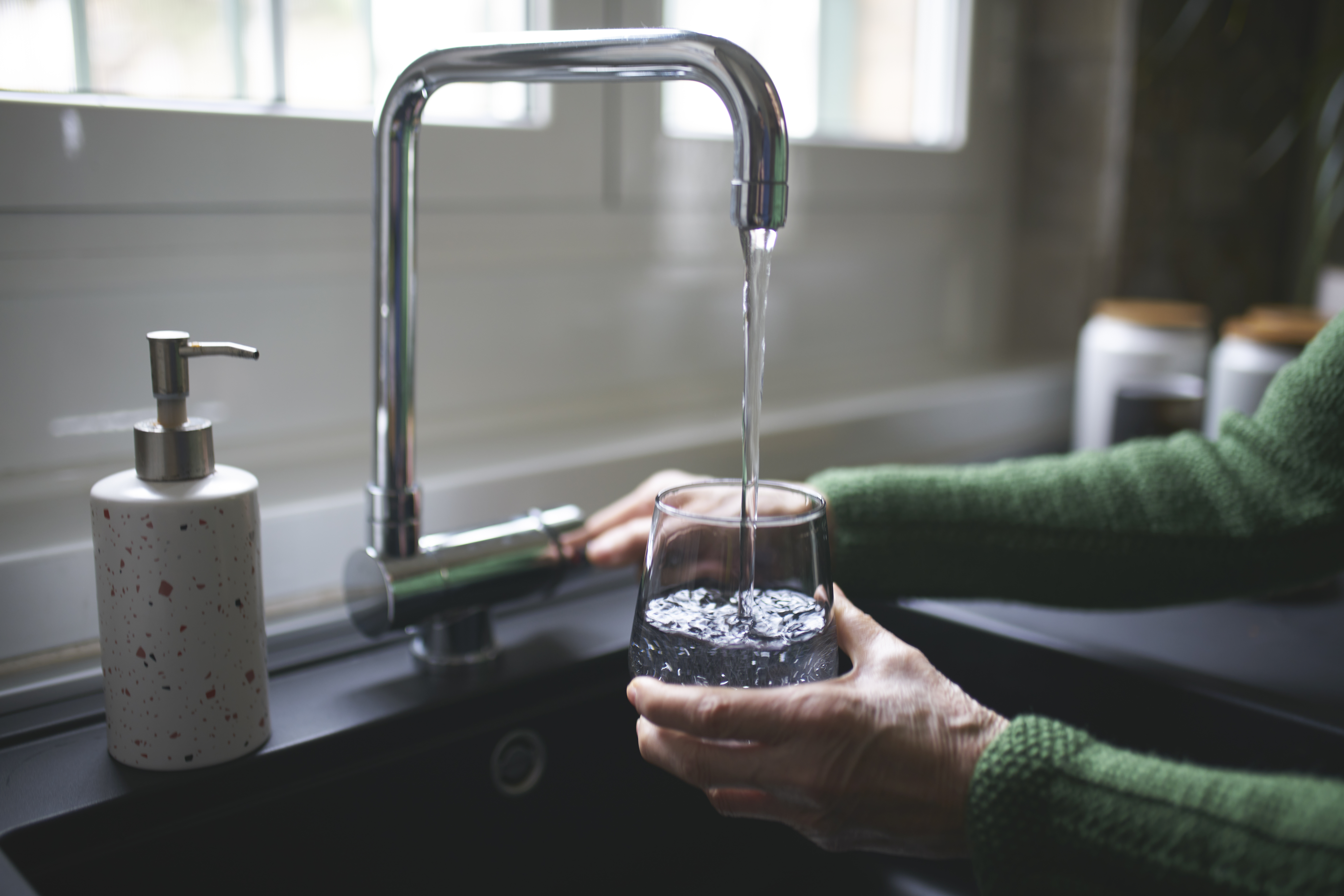 Close up of a woman's hand filling a glass of filtered water from the tap in the kitchen sink at home.