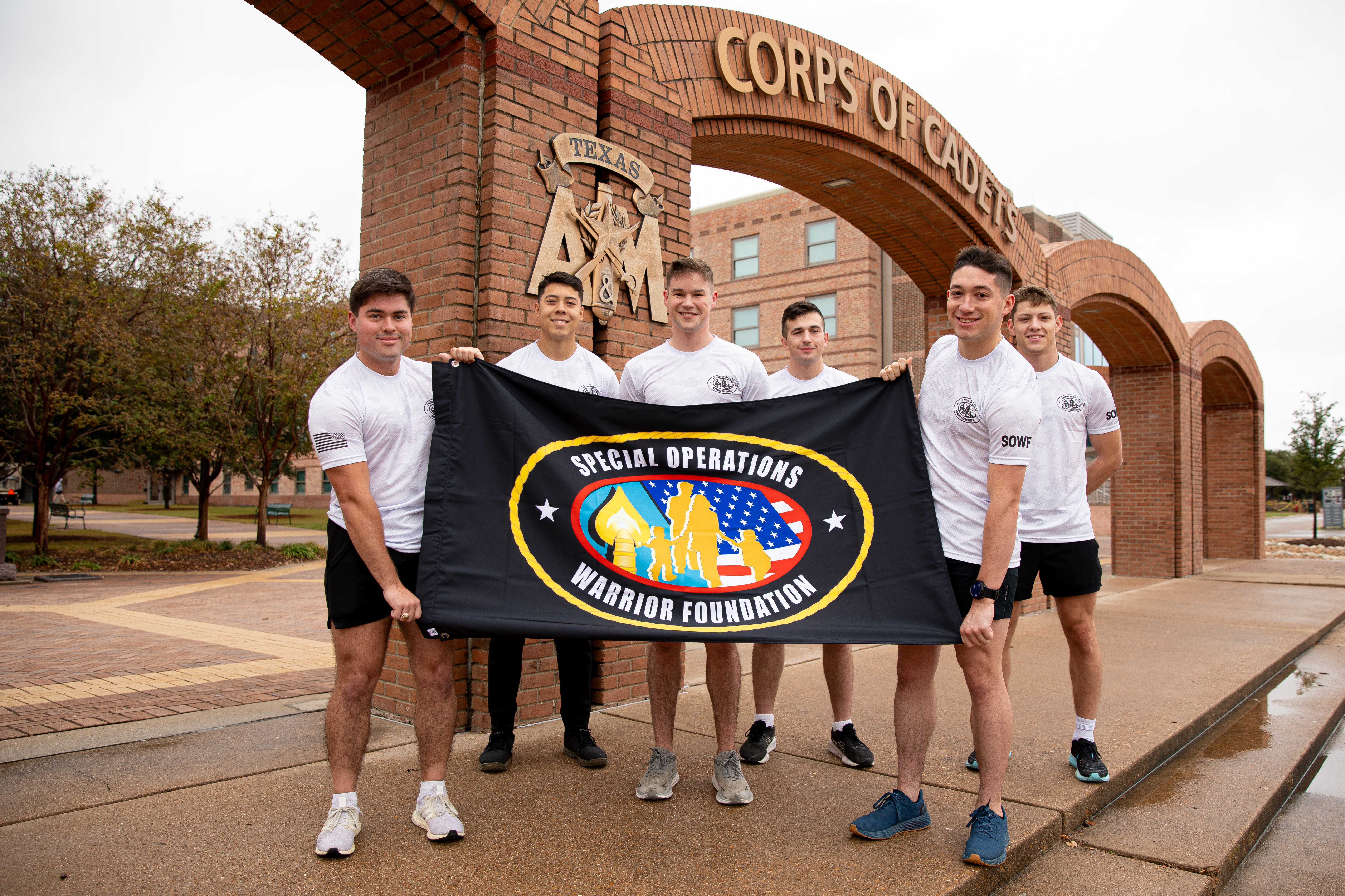 A photo of six members of Texas A&M University's Corps of Cadets standing near the Quad arches while holding a flag for the Special Operations Warrior Foundation.